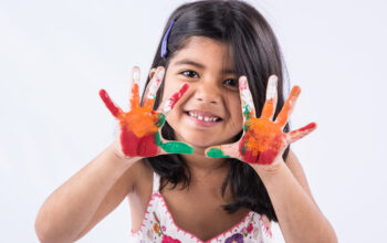 Happy Holi Greeting - Cute little Indian girl with colourful hands, isolated over white background